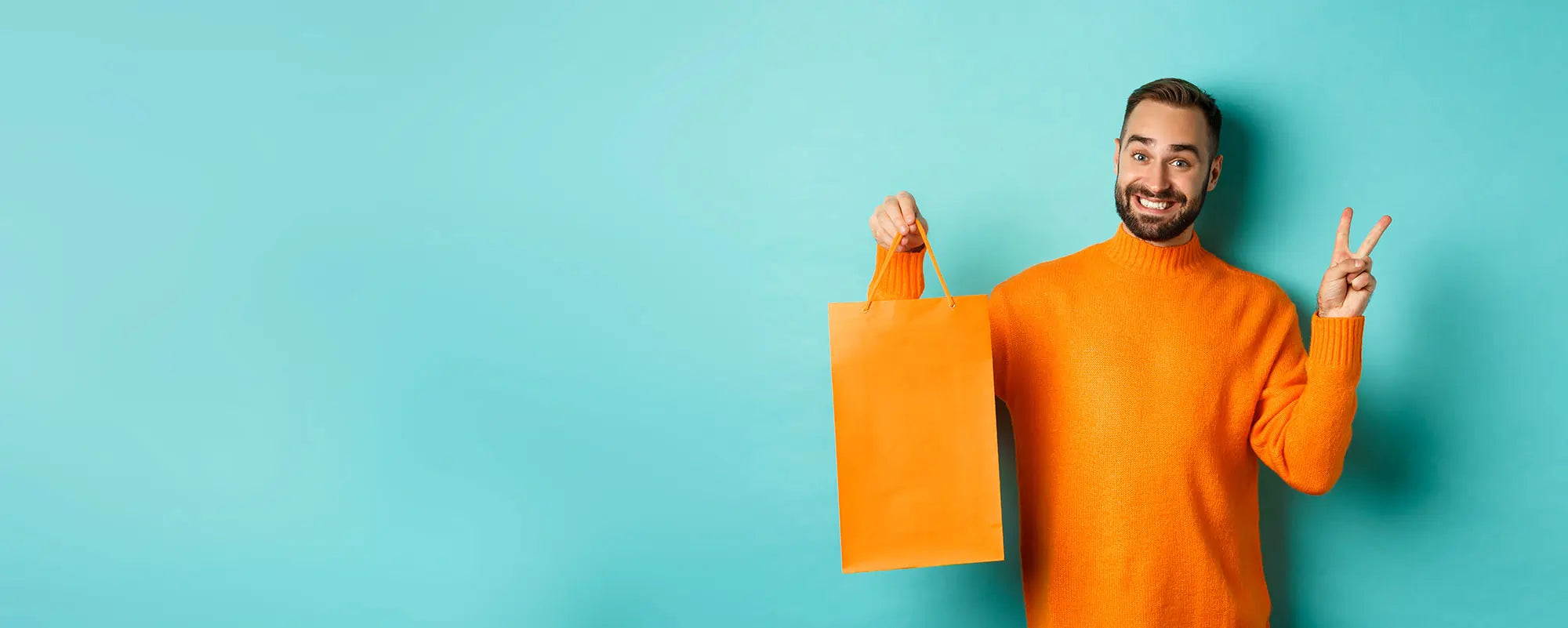 Man with orange sweater holding a shop bag and doing the peace sign